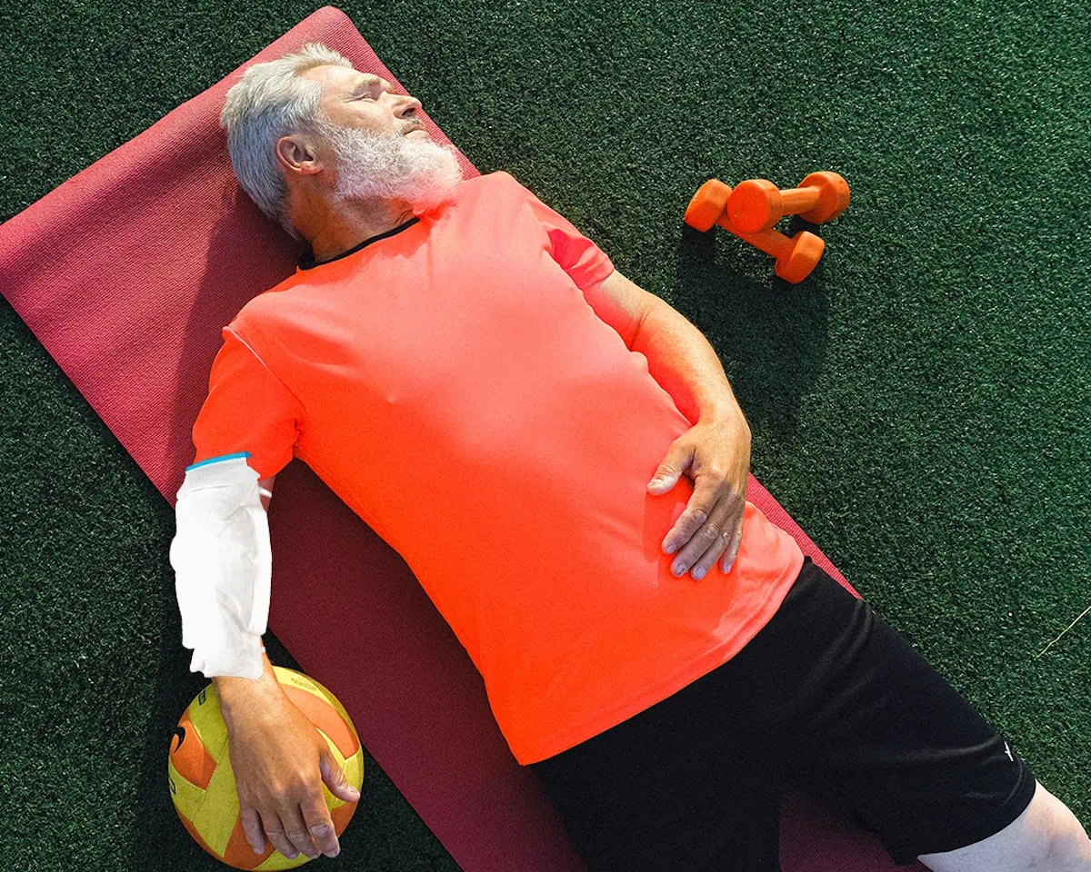 A an wearing an orange shirt reclines on a yoga mat spread out on the lush green grass.